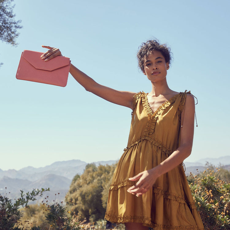 Model in golden minidress holds mini envelope sleeve in pebbled coral